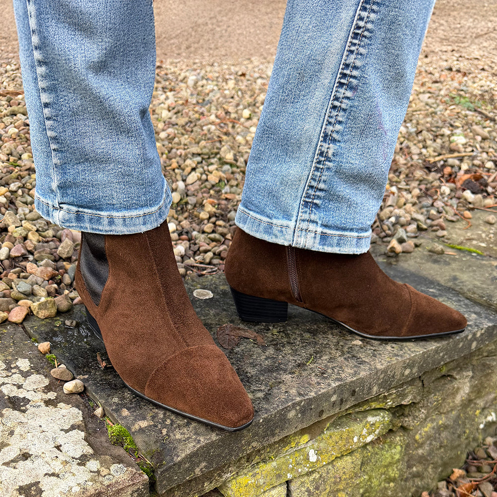Brown suede ankle boots worn with light blue jeans on a stone step.