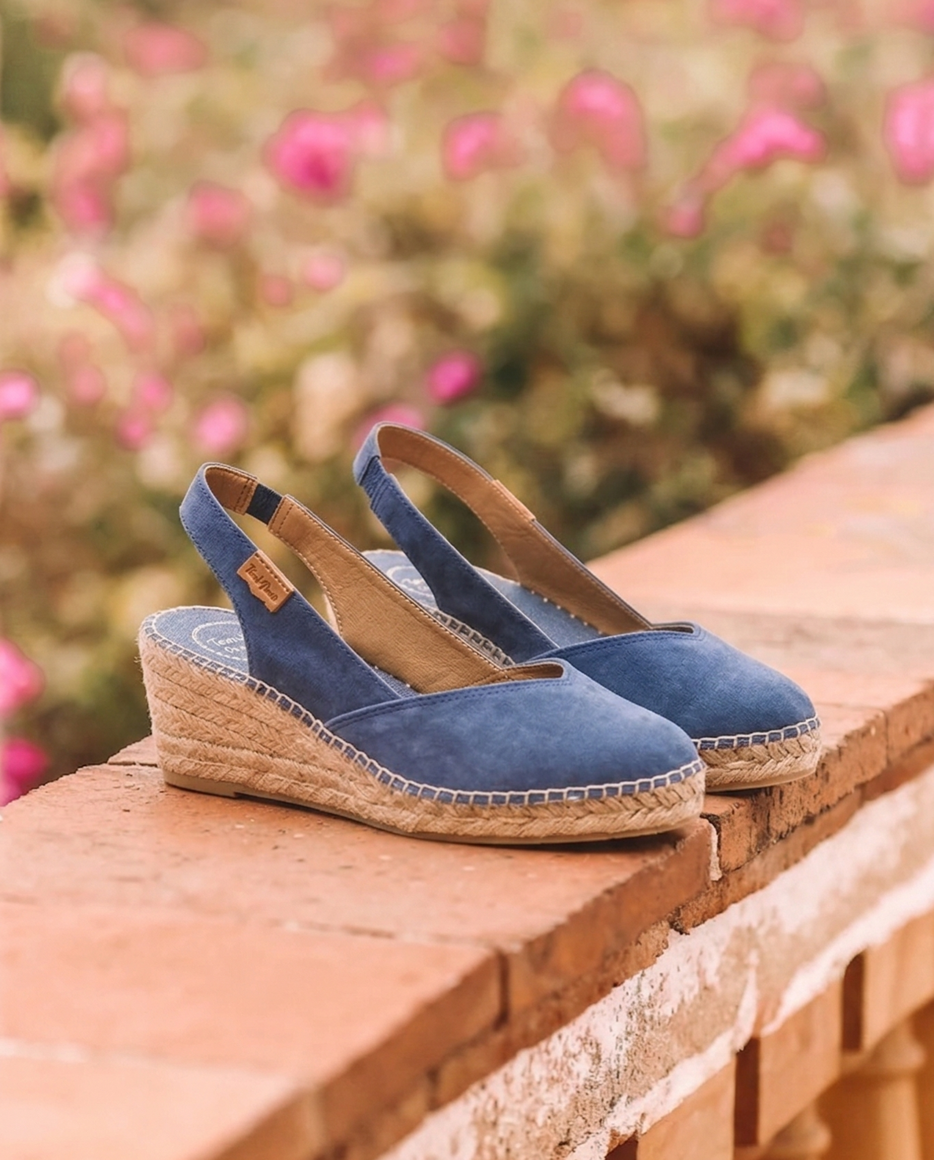 Blue wedge sandals with jute sole on a wooden surface with a blurred floral background