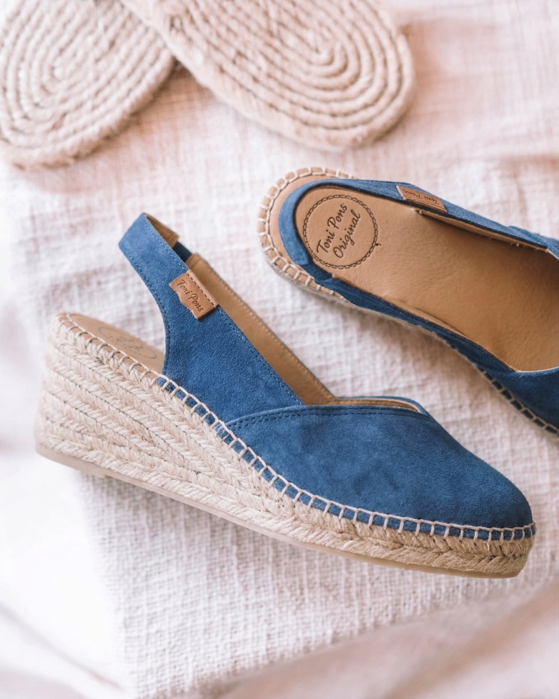Blue wedge espadrilles with jute sole on a light pink textured surface