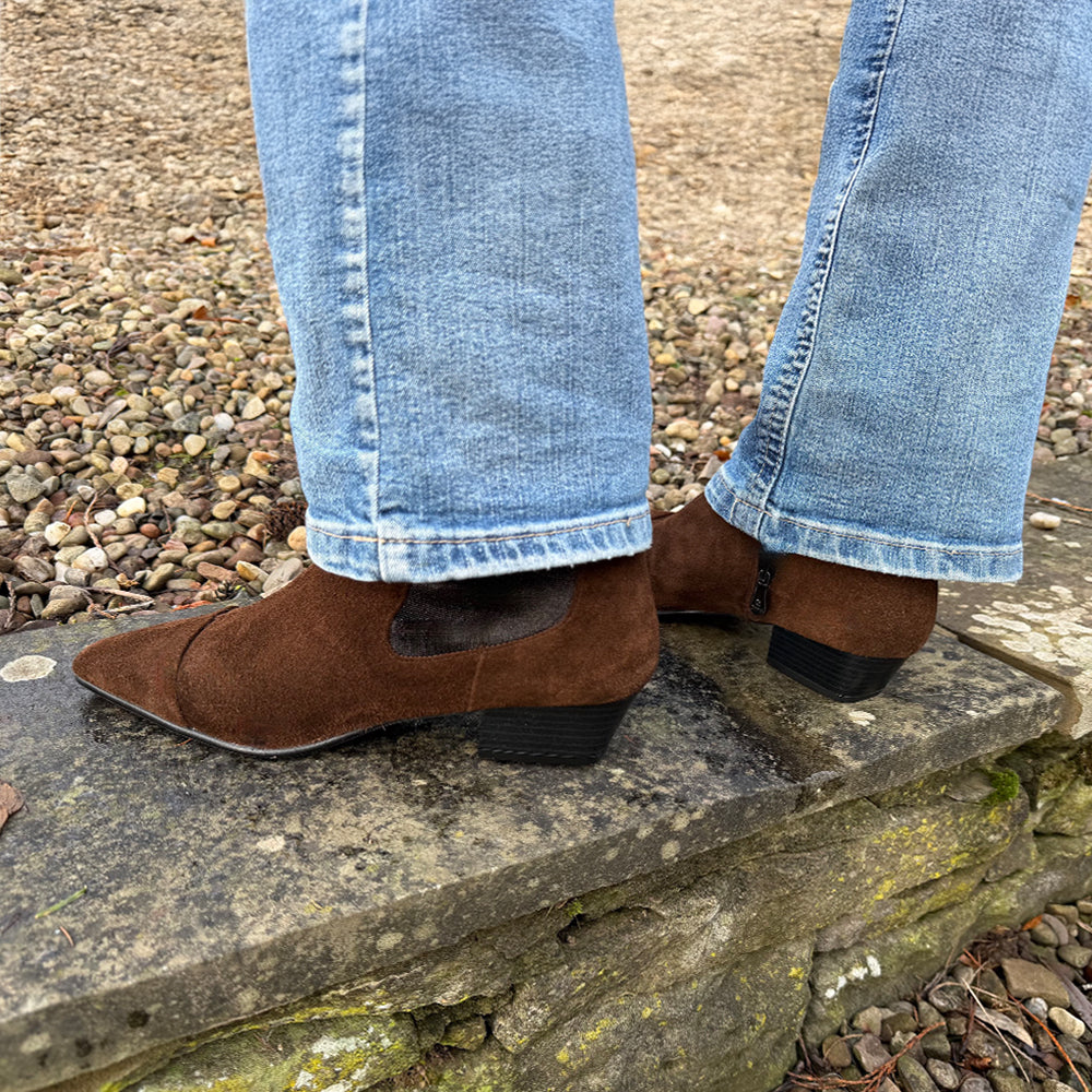 Brown suede shoes worn with blue jeans on a stone step.