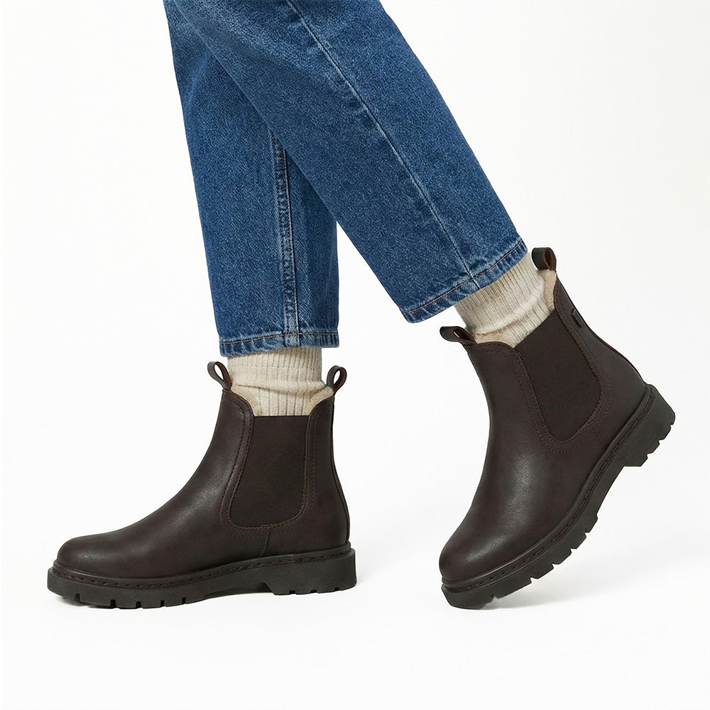 Brown Chelsea boots worn with blue jeans and white socks on a white background