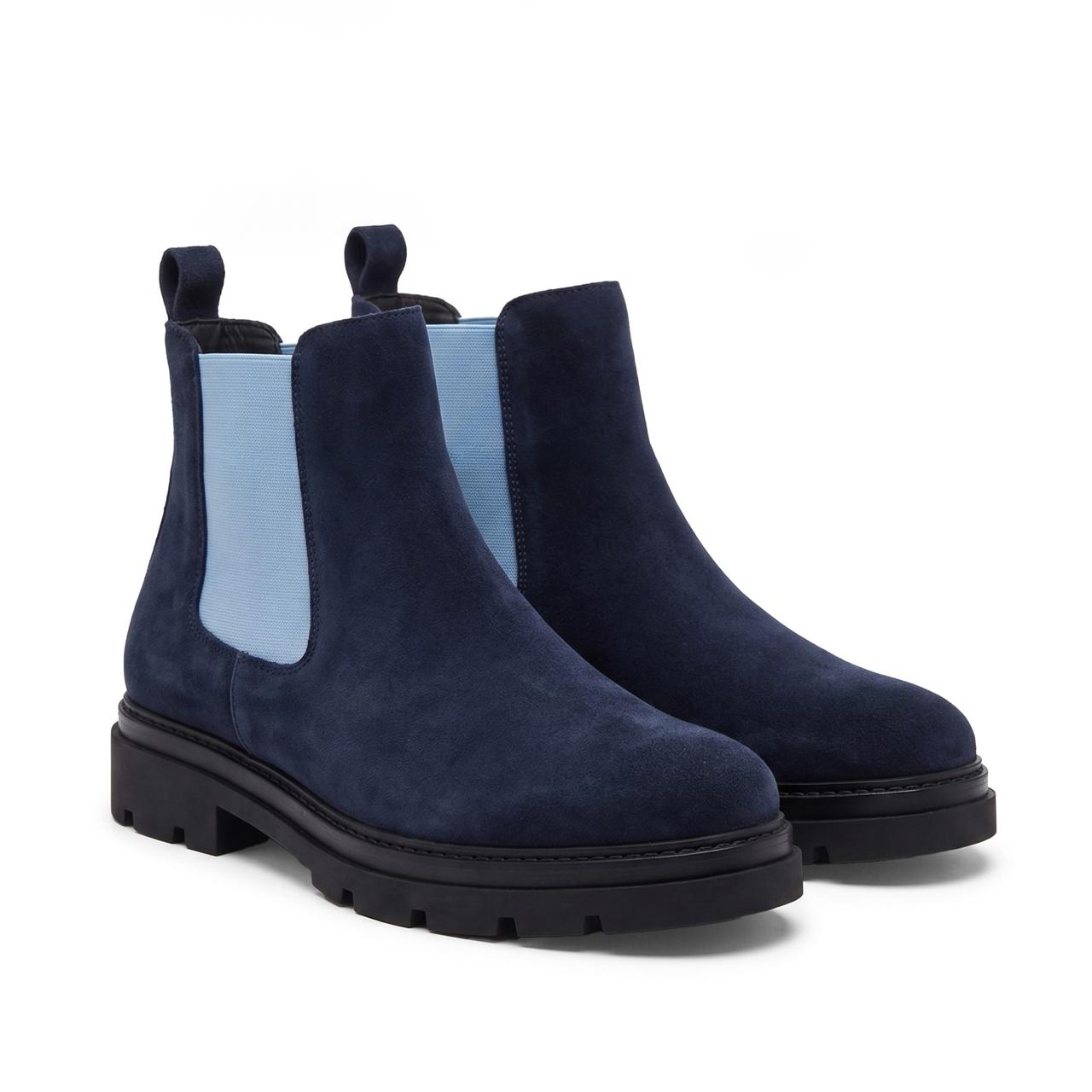 A navy blue pair of suede Chelsea boots with a thick, textured black sole, black laces, and a small white logo on the side, shown against a plain white background.
