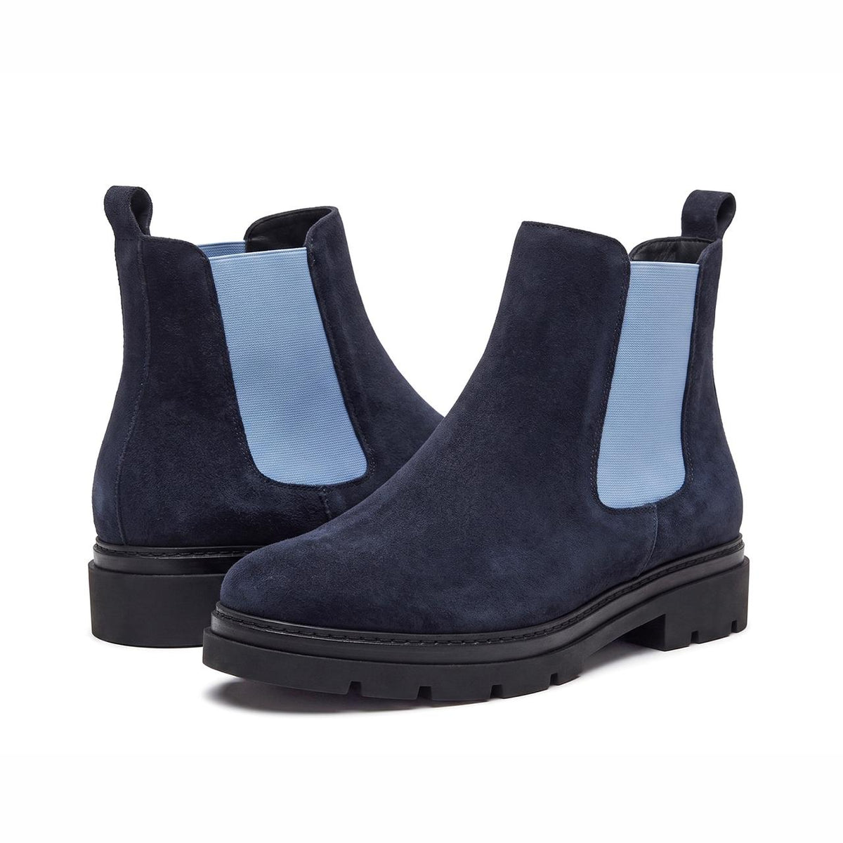 A pair of navy blue suede Chelsea boots with light blue elastic side panels and chunky black soles, shown on a clean white background.