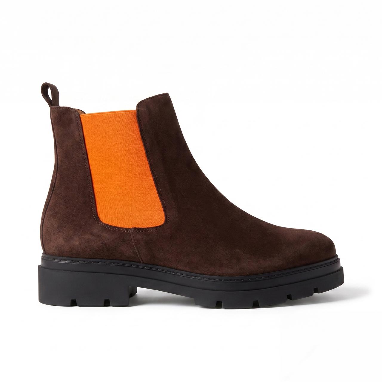 A dark brown suede Chelsea boot with a bright orange elastic side panel and a chunky black lug sole, shown in profile against a white background.