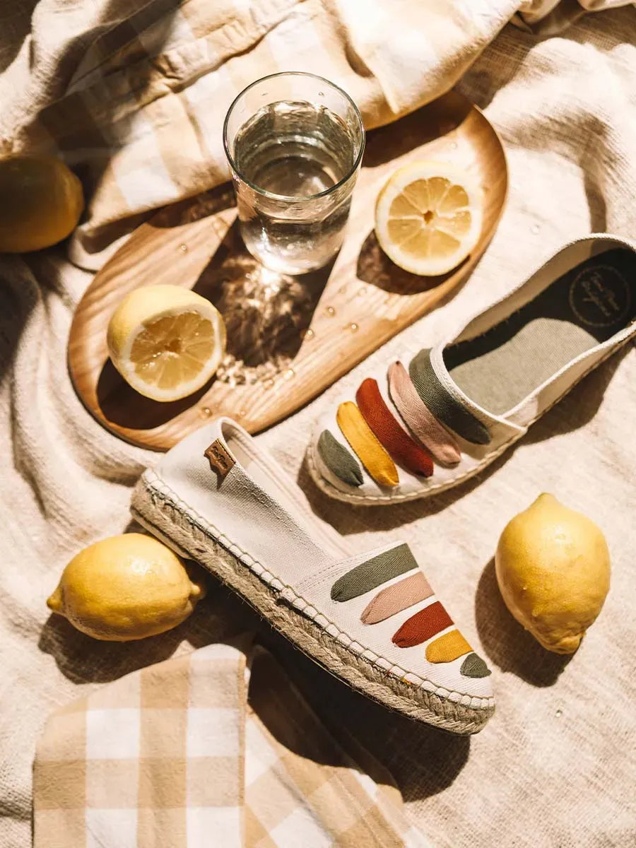 Colourful Espadrille shoes on a fabric background with lemons and water.