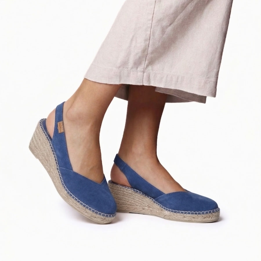 Blue espadrille sandals worn with beige pants on a white background