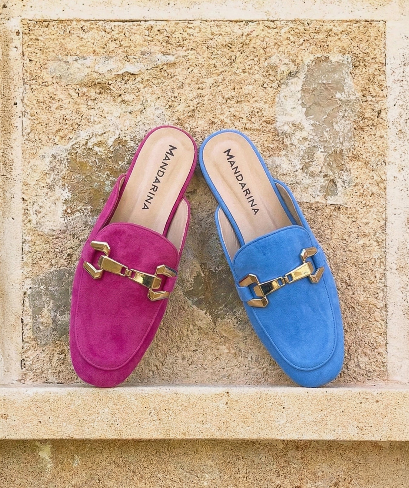 Pair of pink and blue loafers with gold hardware on a textured stone surface