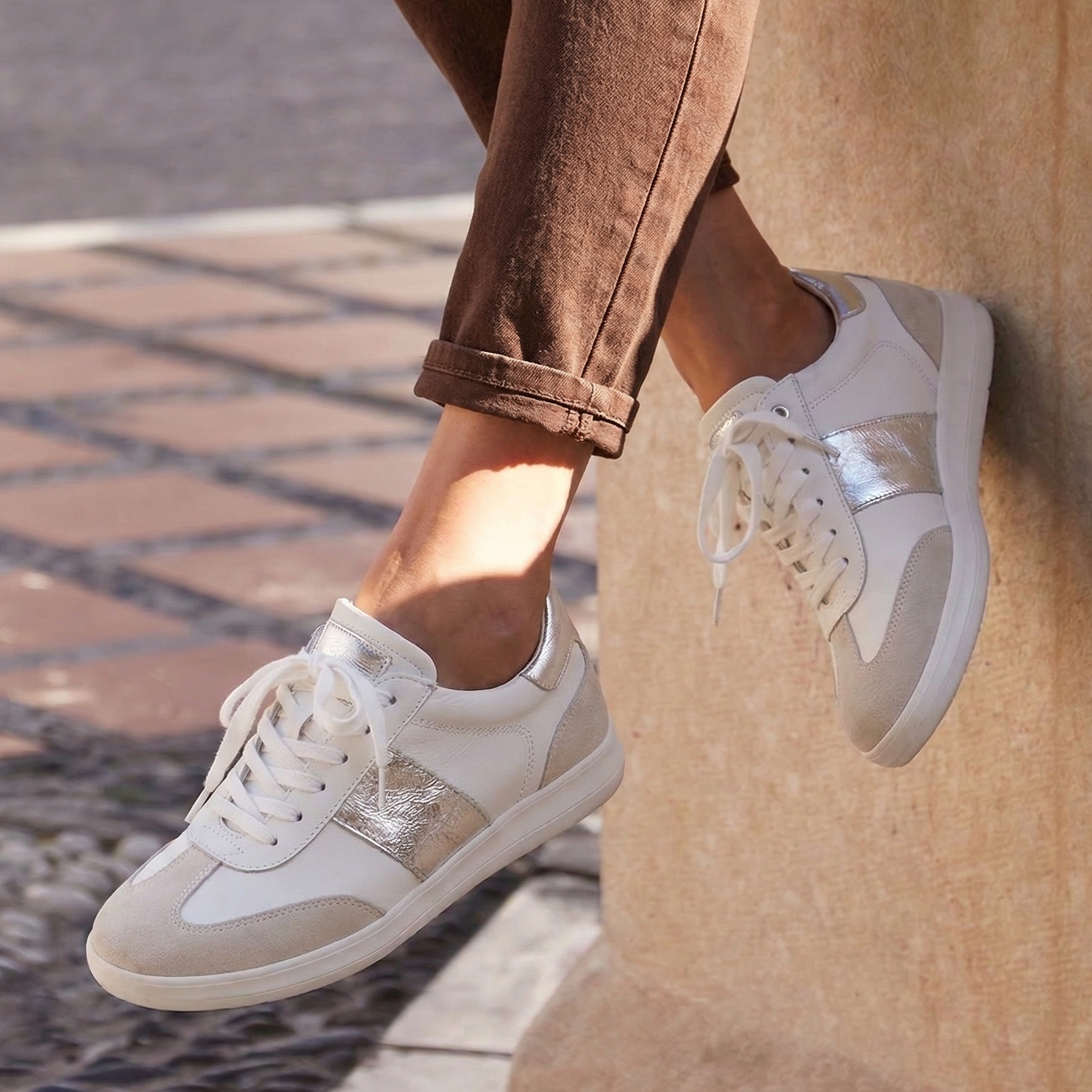 White sneakers worn with brown pants on a stone surface