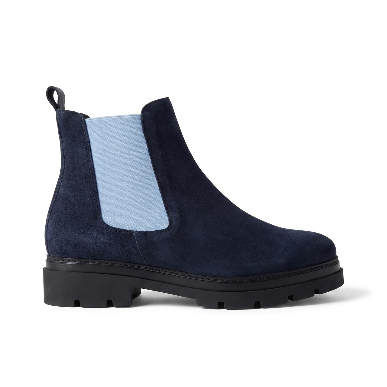 A navy blue suede Chelsea boot with a light blue elastic side panel and a chunky black sole, shown from a side profile on a white background.